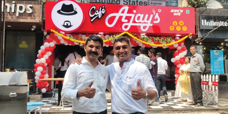 Two men stand in front of an Ajay’s cafe outlet
