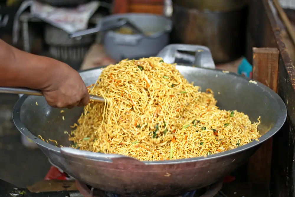 A man tossing vegetable maggi in a big bowl