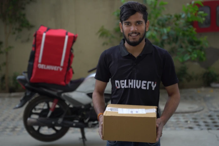 A delivery boy wearing a black tshirt gives a cardboard box parcel to someone